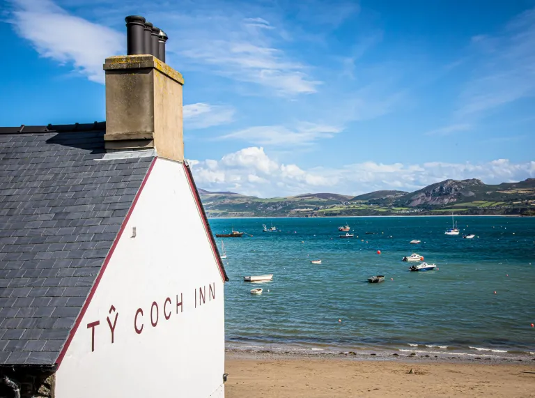 Whitewashed  cottage overlooking a sandy bay with boats and sea views.