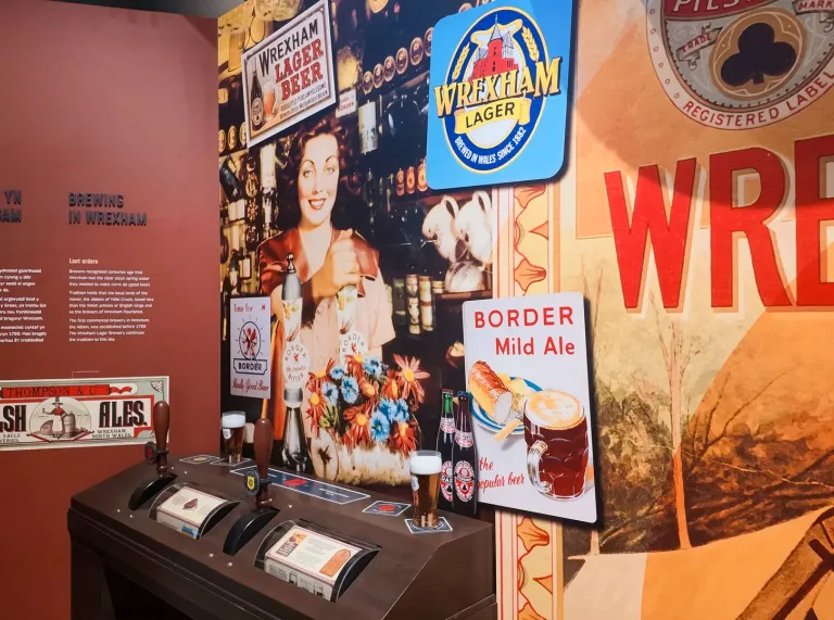 Wrexham brewing history display featuring historic beer advertisements, Wrexham Lager branding, bottles, glasses and brewery memorabilia.