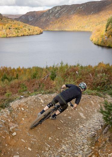 A mountain biker riding downhill with a reservoir and mountains beyond.