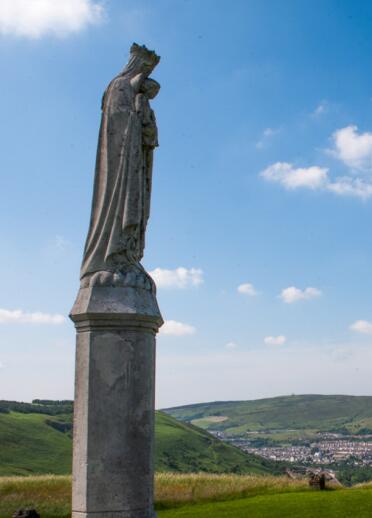 Statue eines Heiligen mit sanften Hügeln und Stadt im Hintergrund.