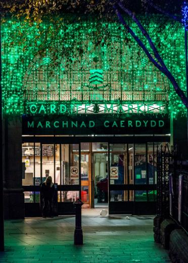 Eingang zur Markthalle von Cardiff bei Nacht, beleuchtet von blau-grüner Weihnachtsbeleuchtung.