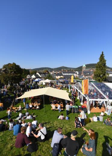 People sitting on a lawn amongst food tents with Abergavenny in the background.