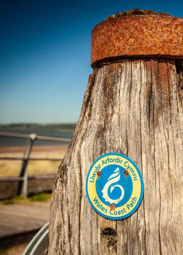 Wales Coast Path Schild auf dem Millennium Coastal Path in Südwales, mit Sand und blauem Himmel.