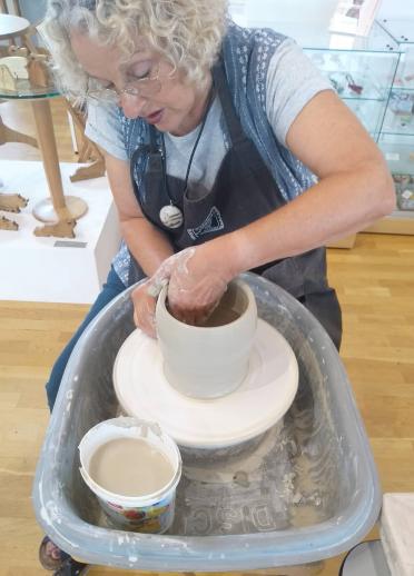 A woman at a potters wheel making a pot