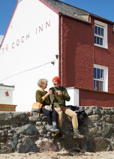Couple sitting on a wall enjoying a drink outside the Ty Coch Inn.
