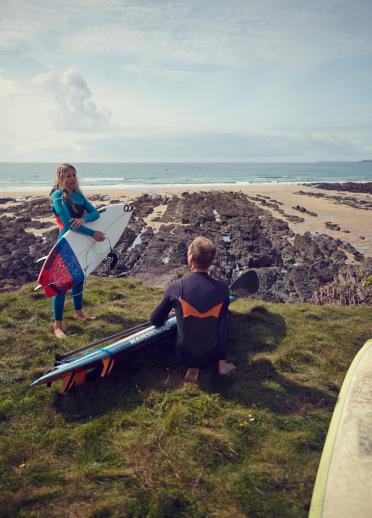 Friends on grass verge by the beach with surfboards ready to go into the water.