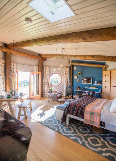 Interior of an eco-cabin with a Welsh blanket covered bed, a laid table and doors wide open.