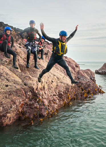 Coasteering group jumping off rocks into sea.