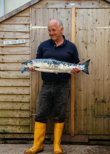 Len Walters, fisherman  in yellow wellies holding large fish infront of his shed