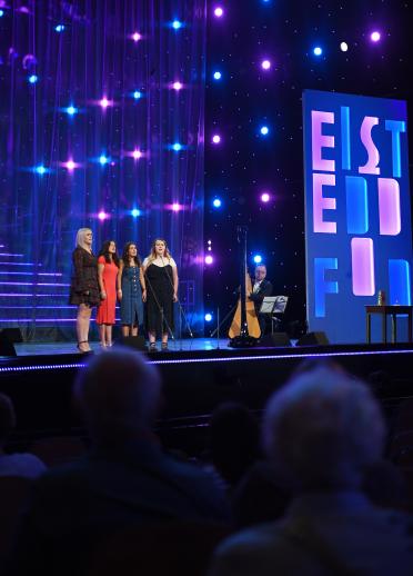 A voice quartet performing on the National Eisteddfod stage with a harp accompaniment