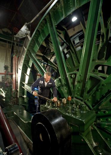 Ein Mann arbeitet an einer Maschine mit einem riesigen grünen Rad im Hintergrund.