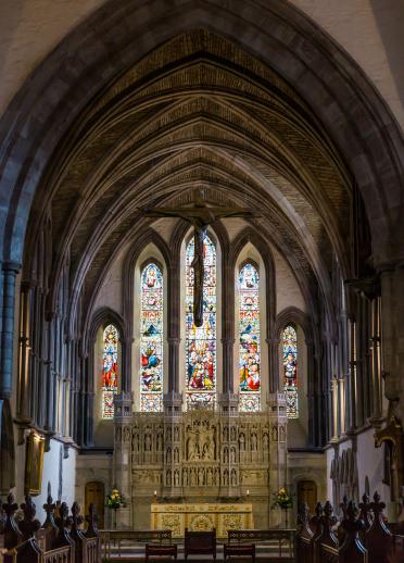Innenansicht eines Bogens in einer Kathedrale mit Altar und einem großen Glasfenster.