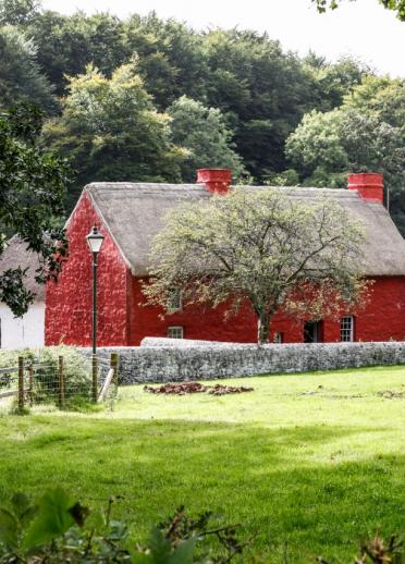 Red cottage next to a field with trees behind 