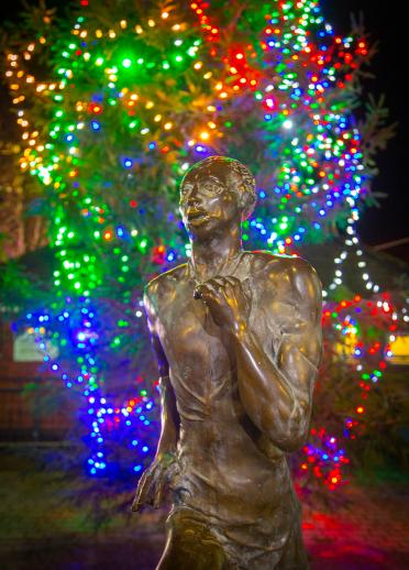 A statue at night with colourful lights behind.