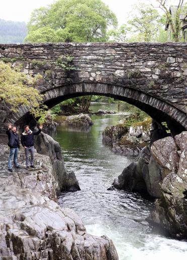 Eine graue Steinbrücke über einen schmalen Fluss.