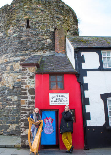 2 musicians, one with harp, outside the Smallest House in Great Britain 