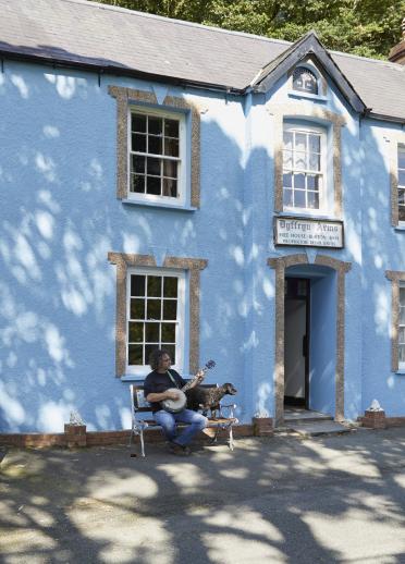 exterior of blue public house with man sat on a bench playing instrument.