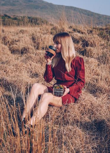  Woman wearing a red dress sitting on the grass drinking coffee