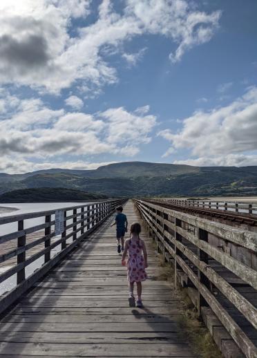 Two children walking on a wooden bridge.