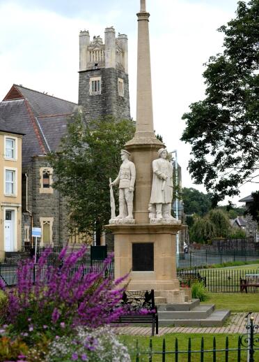 A tall war memorial on a stepped plinth with statues of soldiers around the base. .