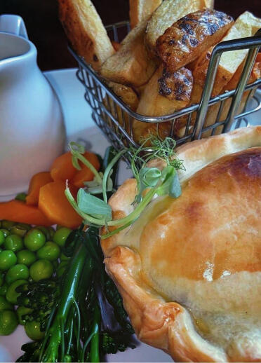 Pie and chips with vegetables and a pot of gravy.