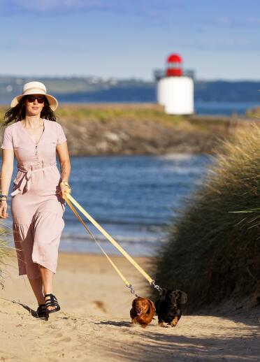 woman walking dogs on beach, with lighthouse in background.