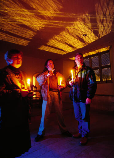 Three men holding candles in a dark and spooky room