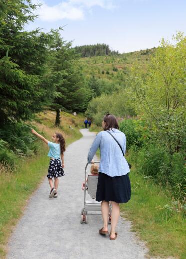 woman pushing pushchair and young girl walking along path with trees.