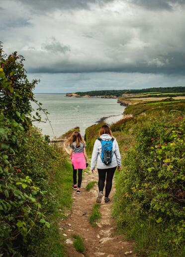 Two people walking along a cliffside coastal path.