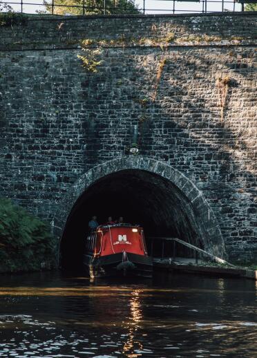 A red narrowboat emerging from a tunnel.