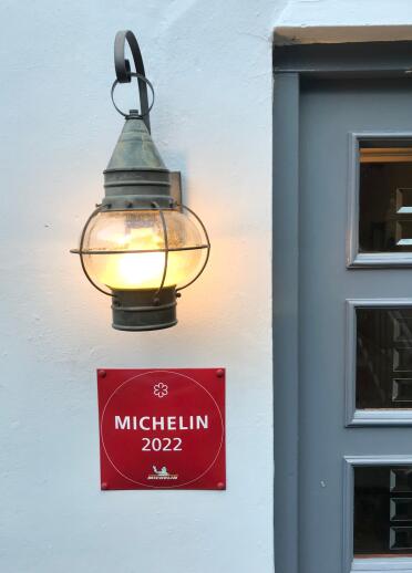 Ein rotes Schild mit der Aufschrift MICHELIN 2022 an einer weißen Hauswand unter einer Lampe.