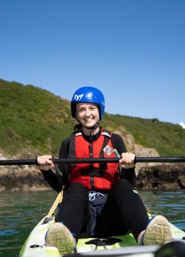 Teenage girl in wetsuit and helmet on a sit on top kayak holding her paddle