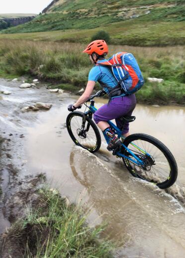 A woman on a mountain bike riding through a muddy puddle.