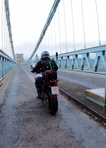 A man on a motorbike crossing a bridge.