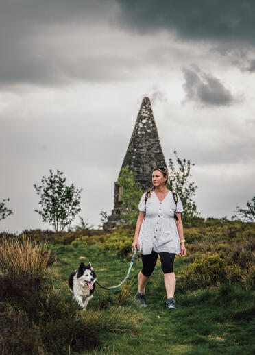 A woman and dog walking in front of a tall pyramidish stone monument.