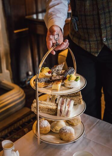 A three tiered stack of plates with a selection of cakes and sandwiches.