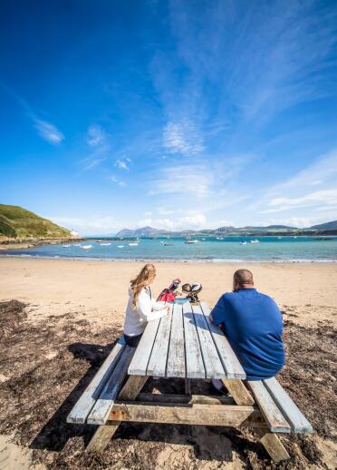 couple sat on wooden bench by beach.