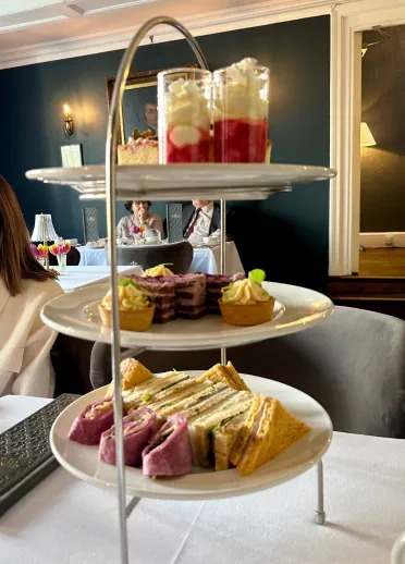 a tiered cake stand of afternoon tea treats including sandwiches, cakes and mini trifles.