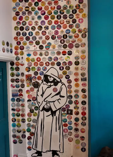 wall in bar with painting of a monk in a white robe surrounded by multiple drink stickers.