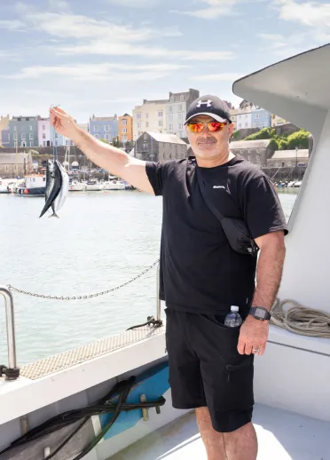 Man on fishing boat holding up mackerel.