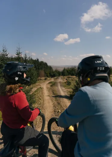 two people wearing helmets on mountain bikes in bike park.