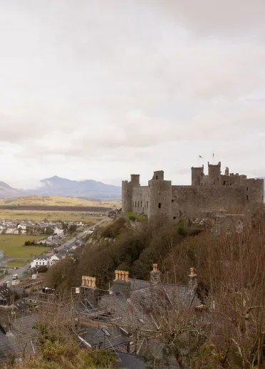 A huge stone castle on a hill, overlooking coast and mountains.