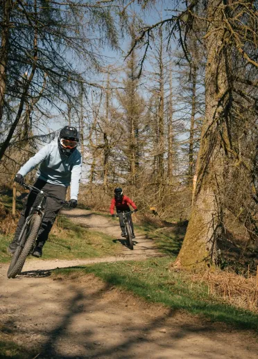 Two people mountain bikes on trail in bike park.