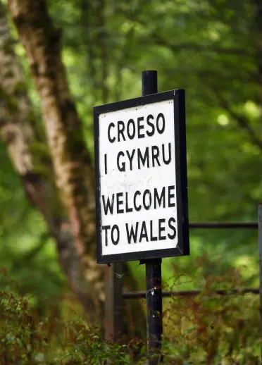 An old metal sign with black letters and a white background stating 'Croeso i Gymru Welcome to Wales'.