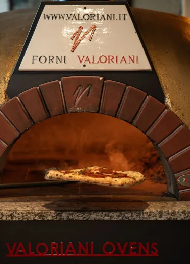 A pizza being placed in the woodfire pizza