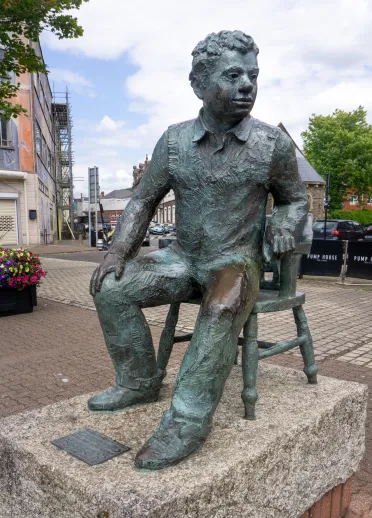 Statue of a man seated on a chair in a city centre square.