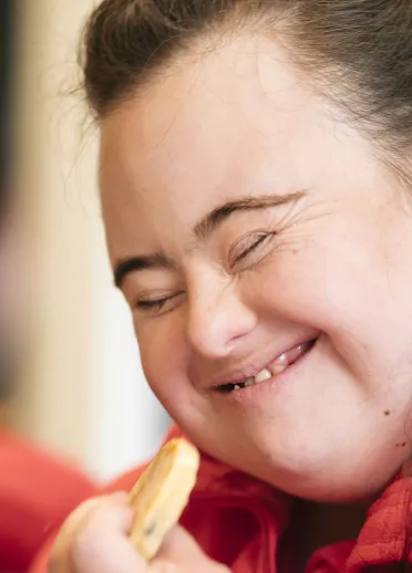 Close-up of a person in a red top holding and eating a Welshcake indoors.