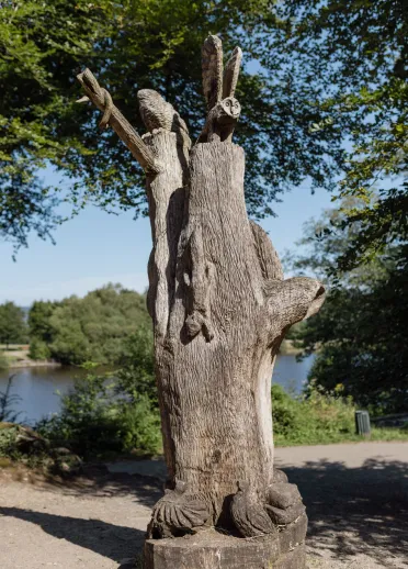 A tall tree stump with carvings including an owl, a squirrel and various birds.