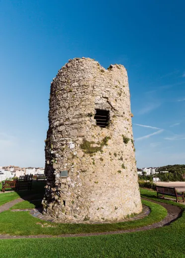 Circular stone tower of Tenby Castle standing on Castle Hill in Tenby, surrounded by grass and overlooking the town and coastline.