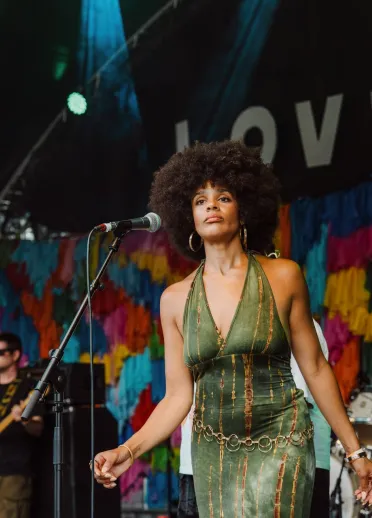 Singer performs on the Big Love Festival stage in front of a colourful backdrop, with band members playing behind.